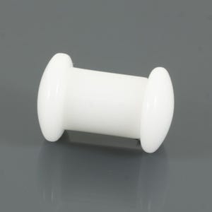 May include: A white, cylindrical object with rounded ends. The object has a smooth, glossy finish, possibly made of plastic. The design is simple and symmetrical, with a central barrel shape and two flared ends. The object is likely a small component.