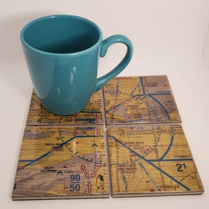 May include: Four square coasters with a wood grain pattern and a map of the Phoenix, Arizona area. The coasters feature landmarks like South Mountain College, Camelback Mountain, and Tempe Lake. The coasters are arranged in a square shape with a teal mug sitting on top.