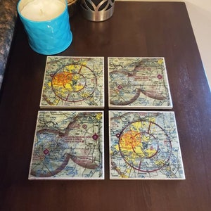 May include: Set of four square coasters featuring vintage-style maps with red, yellow, and orange markings. The coasters are made of a light brown material and have a glossy finish.
