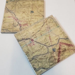 May include: Two vintage-style coasters with a map design. The coasters are made of wood and have a distressed look. The maps show different areas with red markings and numbers. The top coaster shows the number 78 and the bottom coaster shows the number 81.