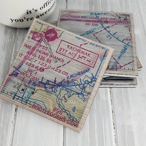 May include: Four wooden coasters with a vintage map design featuring the Kachemak Bay area of Alaska. The coasters feature blue lines representing waterways, red text, and a brown woodgrain background.