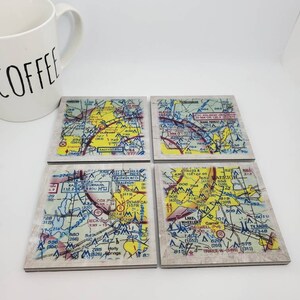 May include: Set of four coasters featuring vintage-style maps of the Raleigh, North Carolina area. Each coaster is made of a light brown material with a white border and features a yellow, red, and blue color scheme.