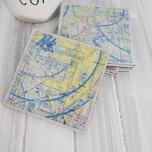 May include: Set of four coasters featuring vintage aeronautical charts. Each coaster is made of a light brown material with a blue, yellow, and white map design. The maps show various details, including flight paths, altitudes, and landmarks. The text on the maps includes "DETROIT METRO WAYNE CO DIW" and "YANDOT".