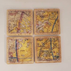 May include: Four square coasters with a map design. Each coaster features a different section of a map with labels like "Wayzata", "Maple", "Victoria", and "Flying Cloud". The coasters are made of a light brown material with a speckled texture.