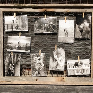May include: A rustic wooden framed photo display with chicken wire backing. Nine black and white photographs are clipped to the wire with small wooden clothespins. The photos depict couples in various romantic poses.