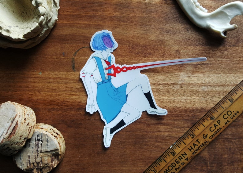May include: A sticker featuring a blue-haired anime character in a white and blue school uniform. The character is depicted with a red chain piercing through their chest, extending off the sticker.