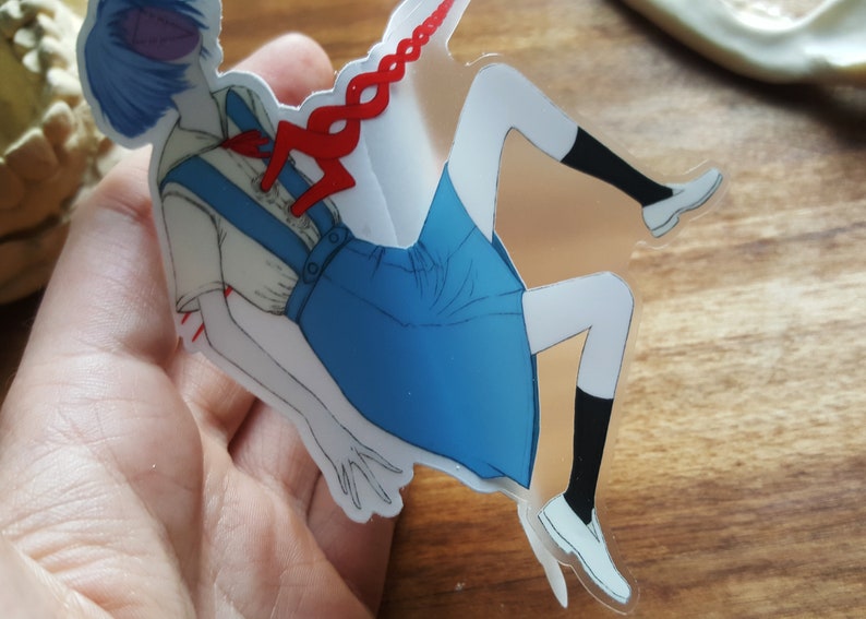 May include: A clear sticker featuring an anime character with blue hair, wearing a white shirt with a blue skirt and red accents. The character is depicted with a red string attached to their chest.