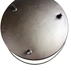 Puede incluir: La parte inferior de una olla de hierro fundido con tres patas. La olla est&aacute; marcada con "14 CO" y "MADE IN USA".