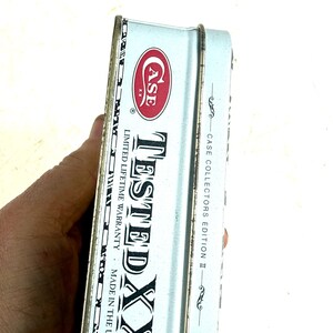 May include: A light blue metal Case XX collector's edition tin. The tin features the Case logo in red and white, with the words "TESTED XX" in large black letters. The text "LIMITED LIFETIME WARRANTY" and "MADE IN THE U.S.A." are also visible.