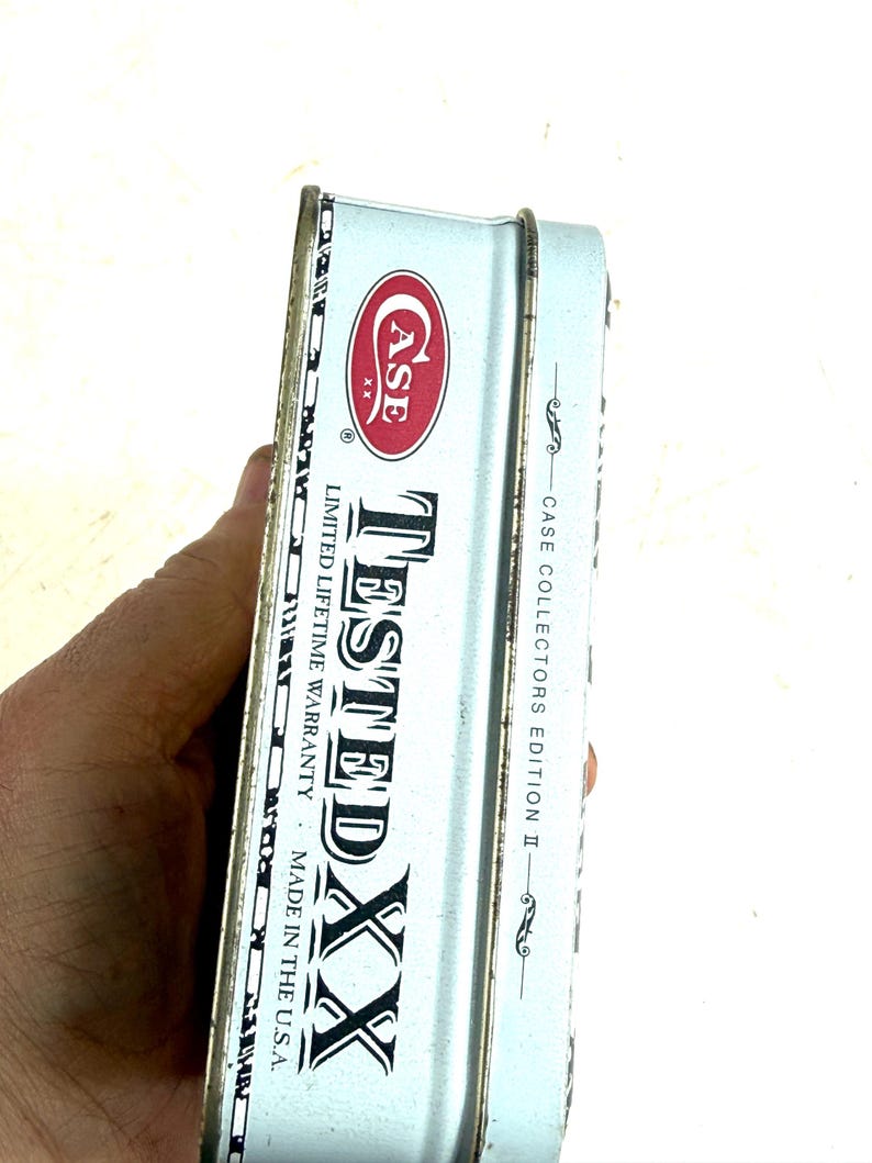 May include: A light blue metal Case XX collector's edition tin. The tin features the Case logo in red and white, with the words "TESTED XX" in large black letters. The text "LIMITED LIFETIME WARRANTY" and "MADE IN THE U.S.A." are also visible.