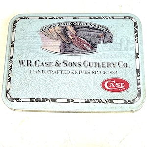 May include: A rectangular, light blue metal tin with the text "HAND-CRAFTED KNIVES SINCE 1889" and "W.R. CASE & SONS CUTLERY CO." The tin features an illustration of a hand holding a knife and the Case logo.