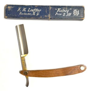 May include: A straight razor with a wooden handle and a silver blade, next to a blue box. The box has the text "F. H. Loeffler Rochester, N. Y." and "Kutezy".
