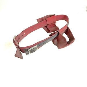 May include: Red work belt with a gray buckle and two attached pouches. The belt is made of a durable material and features a simple design. The belt is designed to be worn around the waist.