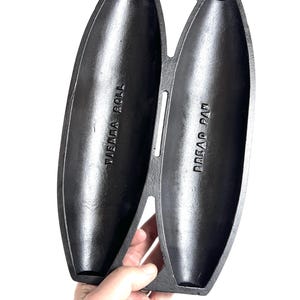 May include: Black cast iron bread pan with two long, oval-shaped molds. The pan is labeled "Bread Pan" and "Vienna Roll".