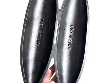 May include: Black cast iron bread pan with two long, oval-shaped moulds. The pan is labelled "Bread Pan" and "Vienna Roll".