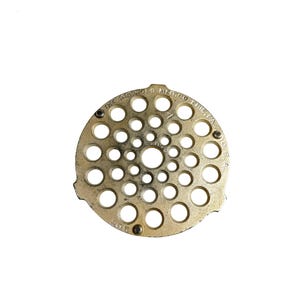 May include: A circular, brass-colored metal object with numerous evenly spaced holes. The text "THE GRISWOLD MFG. CO. ERIE, PA. USA" is visible around the edge. The number "7" is also visible.