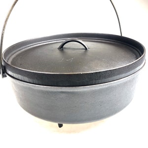 Puede incluir: Una olla de hierro fundido negra con un asa de alambre y tres patas. La tapa tiene una peque&ntilde;a asa y el n&uacute;mero "14" est&aacute; inscrito en la tapa.