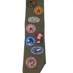May include: A green sash with various embroidered patches, including a red and white patch with the text "Covered Bridge Reservation" and a blue patch with the text "Seneca District Winter Camporee".