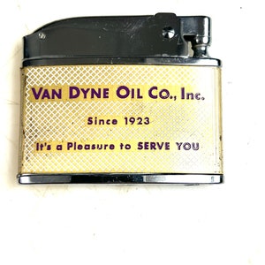 Op de afbeelding: Een goudkleurige aansteker met een zwarte bovenkant en een wit en gouden ruitpatroon. De aansteker heeft de tekst "VAN DYNE OIL CO., Inc. Since 1923 It's a Pleasure to SERVE YOU" erop gedrukt.