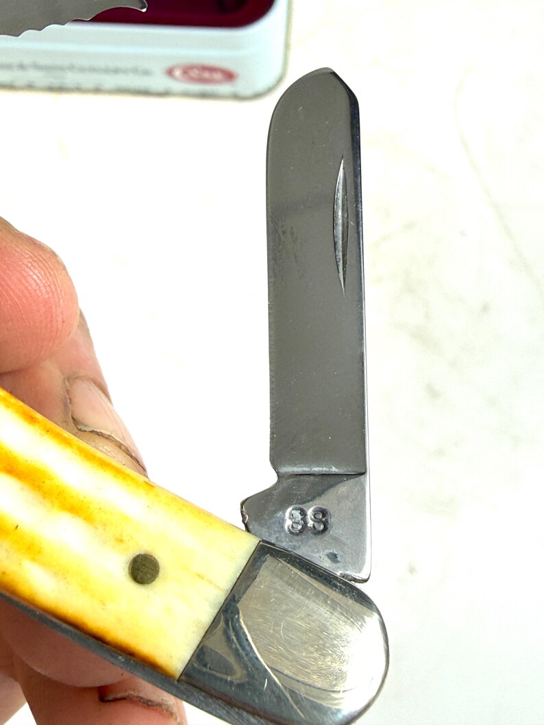 May include: A partially open pocket knife with a stainless steel blade and a handle with a cream and yellow pattern. The blade is marked with the number "88". The knife has a silver bolster and a brass rivet.