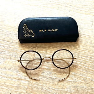 May include: A pair of round, tortoiseshell eyeglasses with gold metal frames and a black leather case with the inscription "J. & J. D.  BUFFALO N.Y.  42" and "MR. W. H. CARY".