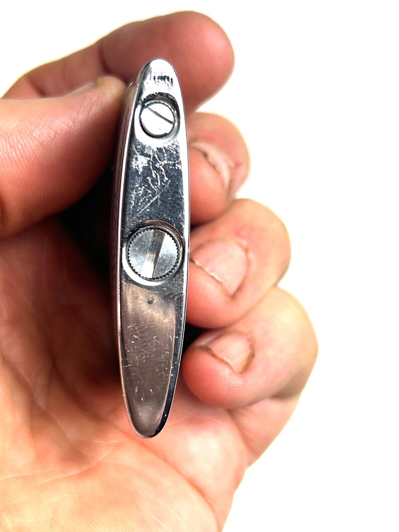 Op de afbeelding: Zilveren aansteker met een getextureerd oppervlak en twee kleine schroeven. De aansteker wordt in een hand gehouden.
