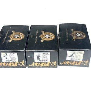 Könnte beinhalten: Drei schwarze Boxen mit goldenen Akzenten, die das Looney Tunes-Logo zeigen. Jede Box hat einen anderen Looney Tunes-Charakter auf der Vorderseite und eine Produktnummer auf der Unterseite. Die Boxen sind Teil der Spotlight-Kollektion.