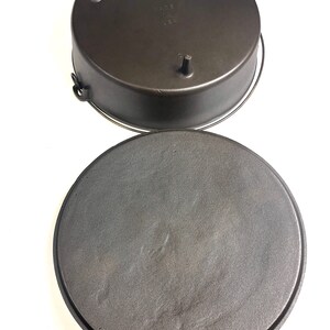 Puede incluir: Una olla de hierro fundido negra con tapa. El fondo de la olla tiene tres patas peque&ntilde;as y la tapa tiene un asa.