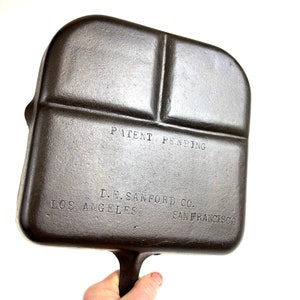 Könnte beinhalten: Eine quadratische Grillplatte aus Gusseisen mit einem Griff. Die Grillplatte hat vier Abschnitte und ist mit "PATENT PENDING D. E. SANFORD CO. LOS ANGELES SAN FRANCISCO" gekennzeichnet.