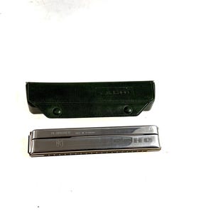 May include: A silver-toned HOHNER harmonica with a dark green leather case. The harmonica is rectangular with visible reeds and the brand name is printed on the top. The case has a snap closure and the word "YACHT" is printed on the top.