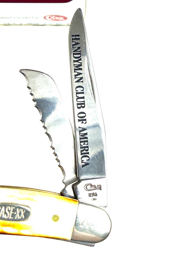 May include: A Case-XX USA pocket knife with a cream-colored handle and two blades. One blade is serrated, and the other is engraved with "Handyman Club of America." The knife is partially open, showcasing the blades.