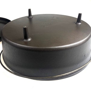 Puede incluir: Cazuela de hierro fundido negro con tres patas y un asa de alambre. El fondo de la olla est&aacute; marcado con el texto "14" y "MADE IN USA".