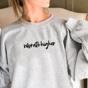 May include: A gray sweatshirt with the text "vibrate higher" printed in black on the front.
