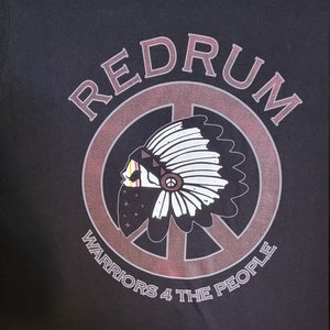 Könnte beinhalten: Schwarzes T-Shirt mit einem rot-weiß-blauen Peace-Zeichen-Motiv. Das Motiv zeigt eine indianische Kopfbedeckung und den Text "REDRUM WARRIORS 4 THE PEOPLE".