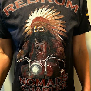 May include: Black t-shirt featuring a graphic of a Native American man wearing a headdress and riding a motorcycle. The text "REDRUM" is printed above the graphic and "NOMADS CHAPTER" is printed below.