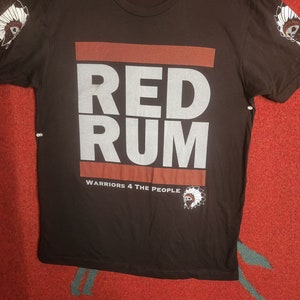 Może przedstawiać: Czarny T-shirt z białym nadrukiem, na którym widnieje napis "RED RUM" i "WARRIORS 4 THE PEOPLE". Nadruk zawiera również indiański strój głowy.