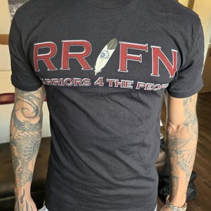 May include: Black t-shirt with a red graphic that says "RR/FN Warriors 4 The People" with a feather design in the middle.