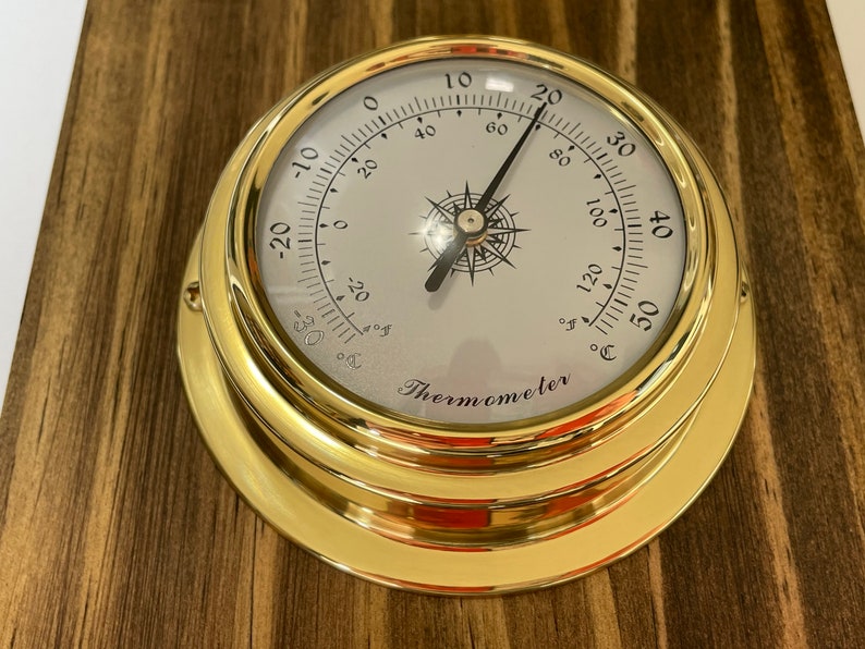Op de afbeelding: Een messing thermometer met een wit gezicht en zwarte markeringen. De thermometer geeft temperaturen aan van -20 tot 50 graden Fahrenheit en Celsius. De thermometer is gemarkeerd met "Thermometer".