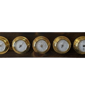 Puede incluir: Un conjunto de cinco indicadores anal&oacute;gicos de color lat&oacute;n montados en una placa de madera oscura. Los indicadores tienen caras blancas con agujas negras y marcas negras.