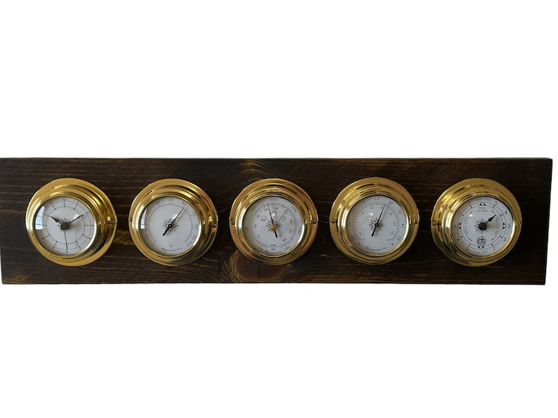 Puede incluir: Un conjunto de cinco indicadores anal&oacute;gicos de color lat&oacute;n montados en una placa de madera oscura. Los indicadores tienen caras blancas con agujas negras y marcas negras.