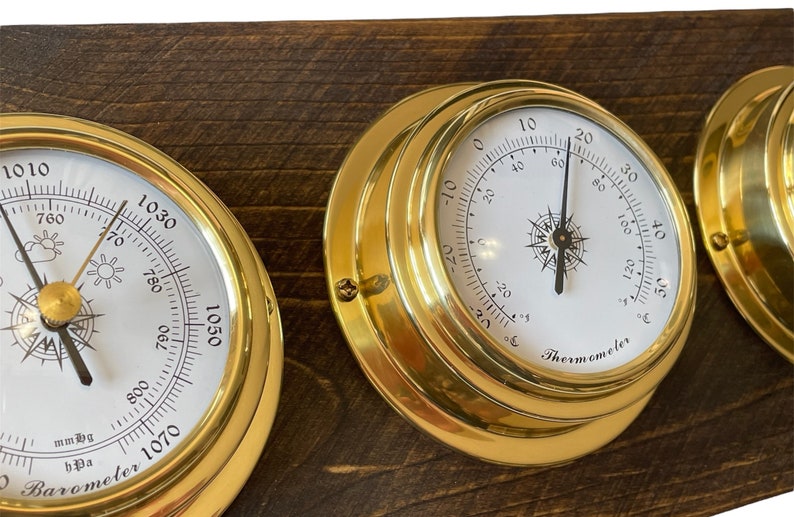 Puede incluir: Un conjunto de tres indicadores n&aacute;uticos de estilo n&aacute;utico de lat&oacute;n montados en una tabla de madera. Los indicadores incluyen un bar&oacute;metro, un term&oacute;metro y un tercer indicador con un dial sin marcar.