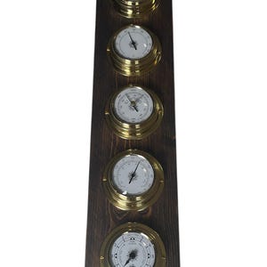 Puede incluir: Un conjunto de cinco instrumentos n&aacute;uticos de lat&oacute;n montados en una placa de madera oscura. Los instrumentos incluyen un reloj, un bar&oacute;metro, un term&oacute;metro, una br&uacute;jula y un reloj de mareas.