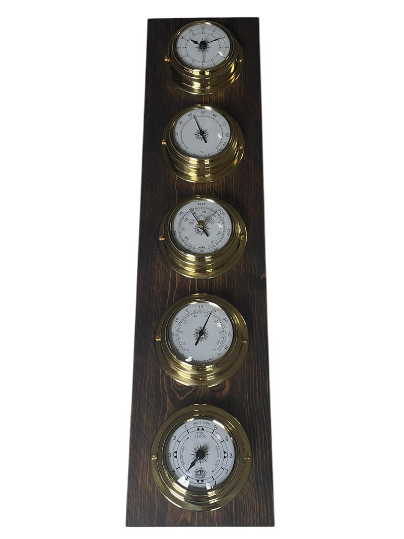 Puede incluir: Un conjunto de cinco instrumentos n&aacute;uticos de lat&oacute;n montados en una placa de madera oscura. Los instrumentos incluyen un reloj, un bar&oacute;metro, un term&oacute;metro, una br&uacute;jula y un reloj de mareas.