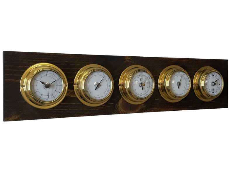 Puede incluir: Un conjunto de cinco indicadores anal&oacute;gicos de color lat&oacute;n montados en una tabla de madera marr&oacute;n oscuro. Los indicadores incluyen un reloj, un bar&oacute;metro y otros tres indicadores con diferentes marcas.