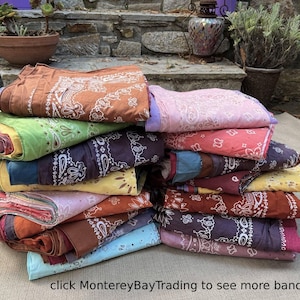 May include: A stack of folded bandanas in various colors, including brown, green, purple, pink, and yellow. Each bandana features a white paisley design. The text "click MontereyBayTrading to see more bandanas!" is visible at the bottom.