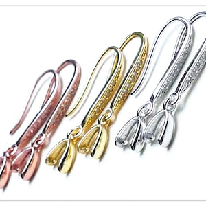 May include: A collection of four pairs of earrings in various metallic finishes: rose gold, gold, and silver. Each earring features a curved hook and a tulip-shaped charm. The hooks are adorned with small, sparkling accents.