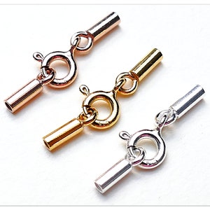 Könnte beinhalten: Drei unterschiedlich farbige Metallverschlüsse zum Schmuckmachen. Die Verschlüsse sind silber, gold und roségold. Jeder Verschluss hat einen runden Ring und ein gerades Rohr.