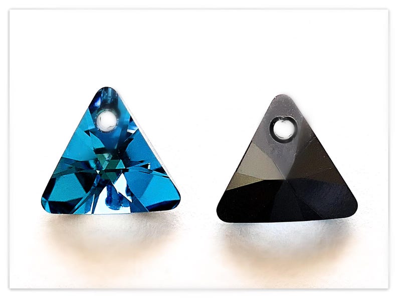May include: Two triangle-shaped crystal pendants with a hole at the top for stringing. One pendant is a dark blue color and the other is black.