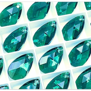 May include: A close-up of a collection of emerald green teardrop-shaped crystal beads with a hole at the top for stringing. The beads are arranged in a grid pattern on a white background.