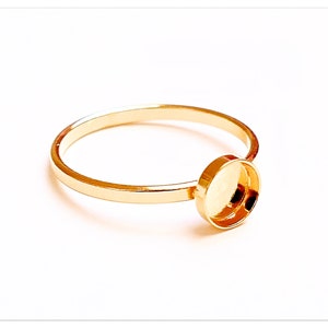 Könnte beinhalten: Ein goldener Ring mit einer runden Zargenfassung für einen Cabochon-Stein.
